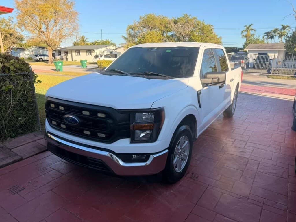 White Ford F-150 crew cab on a red driveway, front three-quarter view